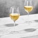 Two Della Luce Maia wine glasses filled with white wine on a marble table.