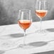 Two Della Luce Maia wine glasses filled with pink wine on a marble table.